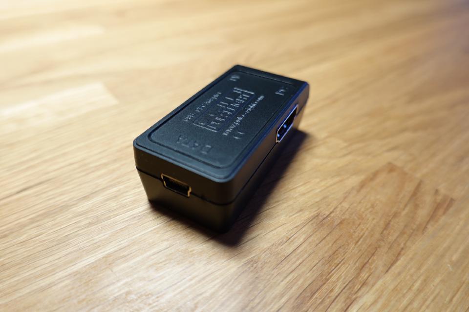 A small black electronic device with a USB and HDMI port lying on a wooden table.